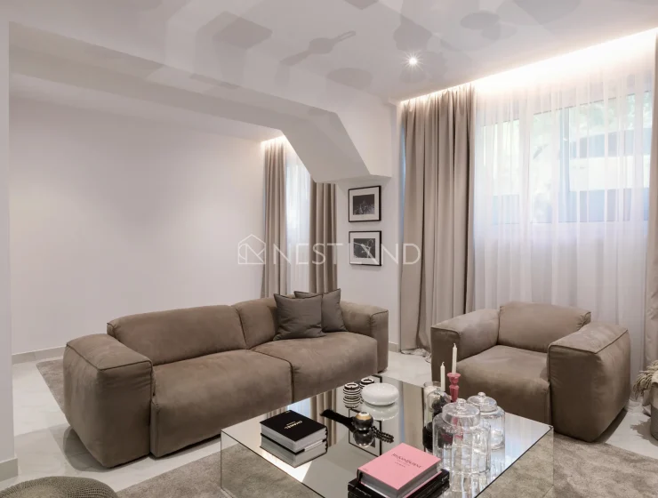 Modern living room with a taupe sofa set, glass coffee table, and sheer curtains.