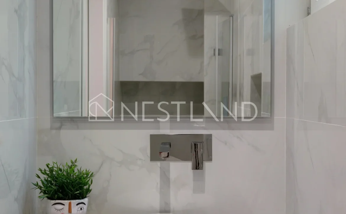 A modern bathroom with marble walls, a white basin, and a decorative plant pot.