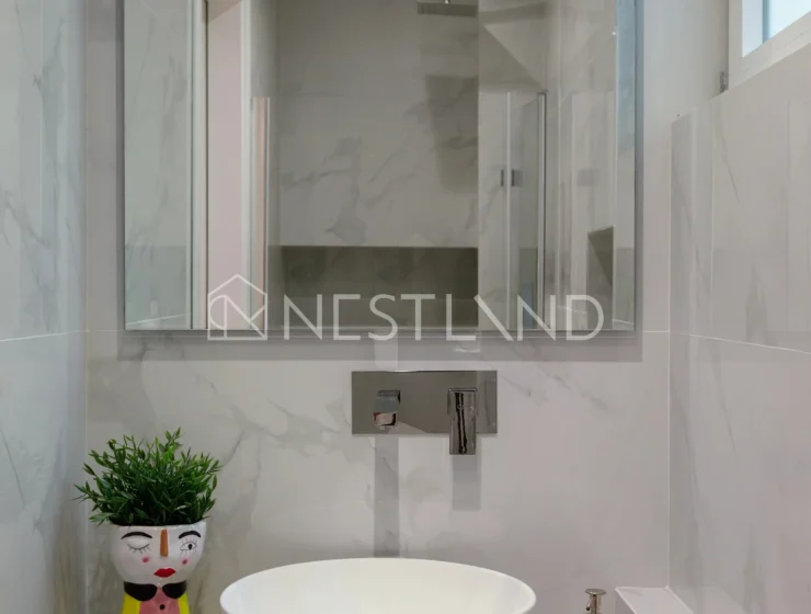A modern bathroom with marble walls, a white basin, and a decorative plant pot.