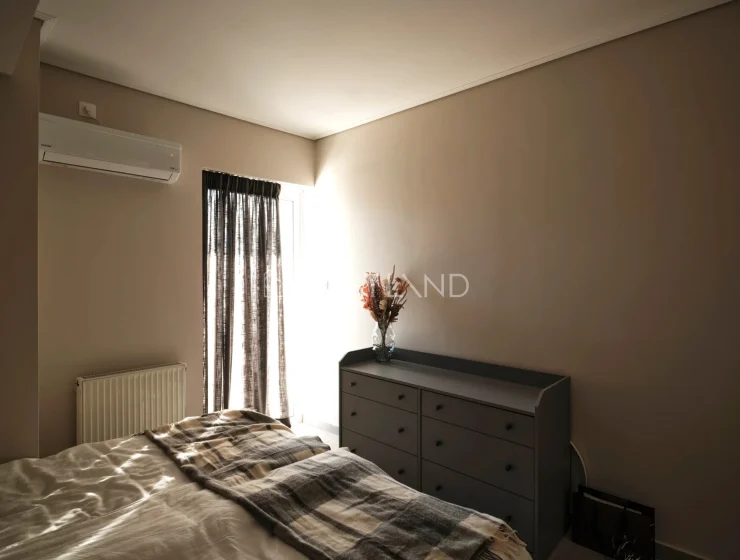 A minimalist bedroom with beige walls, a bed with checkered blanket, a grey dresser, and curtains.