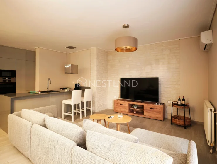 Modern living room with sofa set, TV, kitchen area, and stone accent wall.