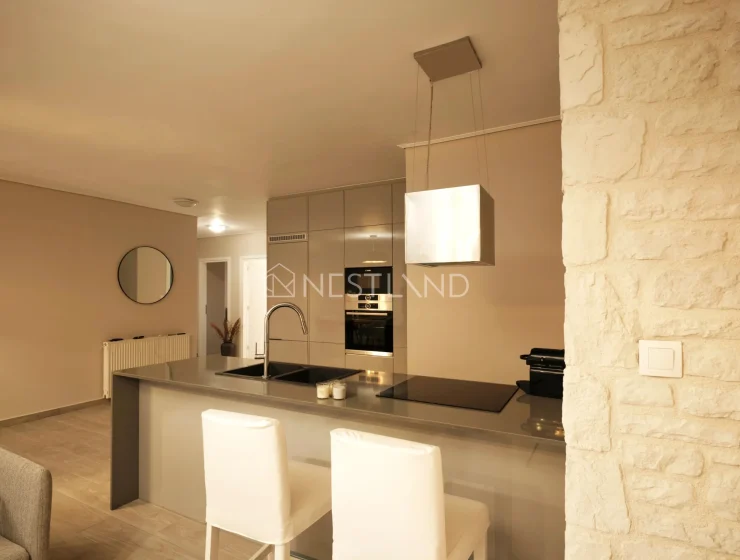 Modern kitchen interior with beige cabinets, built-in appliances, and a breakfast bar with stools.