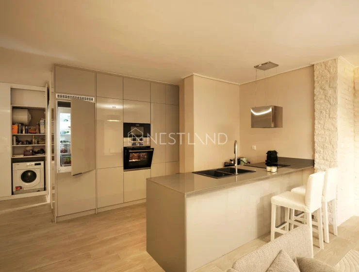 Modern kitchen with beige cabinets, integrated appliances, and a breakfast bar with stools.