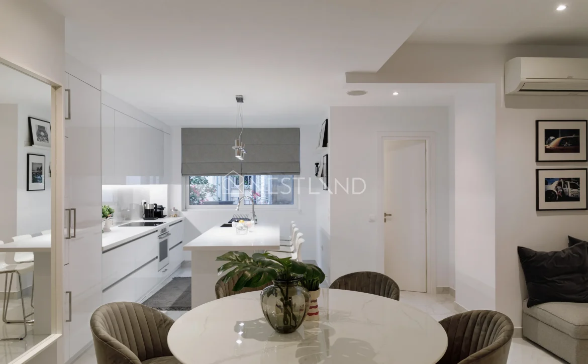 Modern kitchen with white cabinets, marble table, and velvet chairs, view of a window and couch.