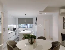 Modern kitchen with white cabinets, marble table, and velvet chairs, view of a window and couch.
