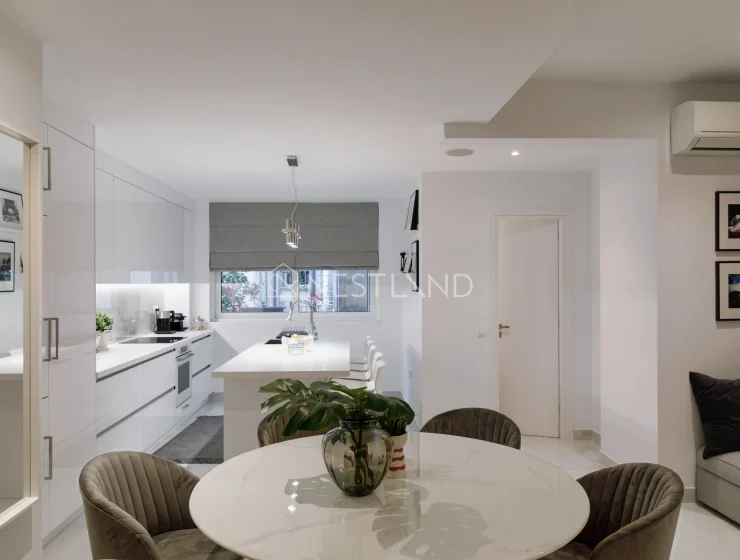 Modern kitchen with white cabinets, marble table, and velvet chairs, view of a window and couch.