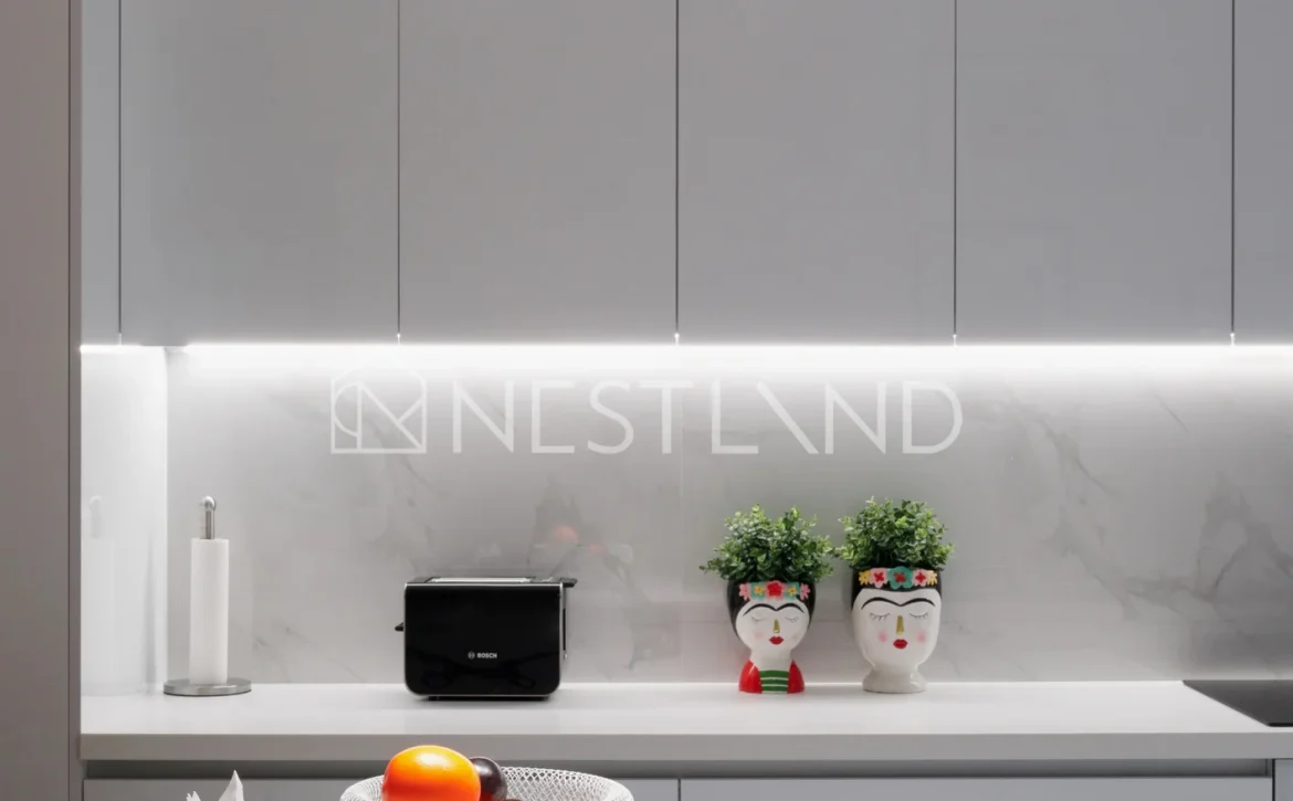 A modern kitchen counter with fruit bowl, plants, and pendant lights.