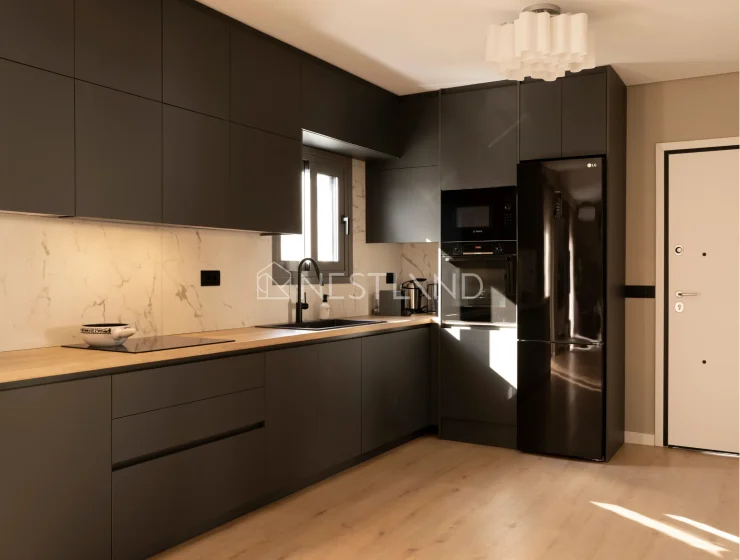 Modern kitchen with dark cabinets, marble backsplash, and sunlight streaming onto a wooden floor.