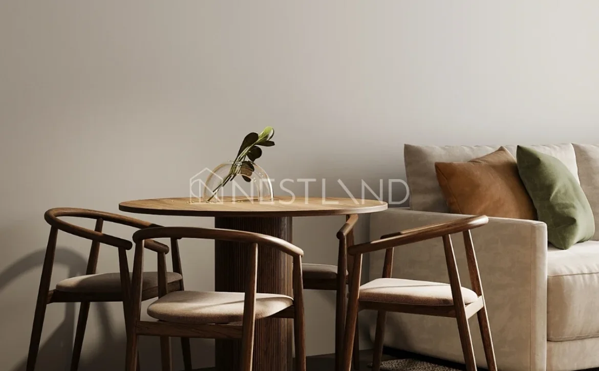 A cozy dining area featuring a round wooden table, three wooden chairs, and a large lamp above, with a soft couch in the background.