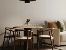 A cozy dining area featuring a round wooden table, three wooden chairs, and a large lamp above, with a soft couch in the background.