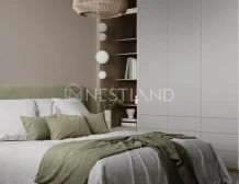 Modern bedroom featuring a cozy bed with gray and green bedding, a woven pendant lamp, and minimalist shelving against a soft beige wall.
